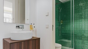 Une salle de bain avec un lavabo blanc, un meuble-lavabo en bois et une cabine de douche aux carreaux verts.