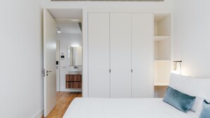 Une chambre avec un grand lit, une armoire blanche et une salle de bain visible à travers une porte ouverte.