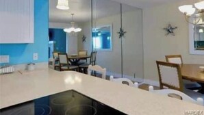Een moderne keuken met een centraal eiland, hangende lampen en een eethoek met stoelen en een tafel.
