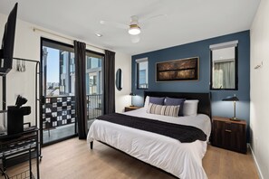 Una camera da letto moderna con un letto grande, una ventola a soffitto, vista sulla città dalla finestra e un balcone con ringhiera in metallo nero.