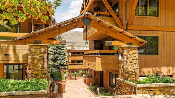 A wooden lodge with a stone entrance, a covered walkway, and a view of the surrounding forest. - Fasching Haus 03 (Aspen)