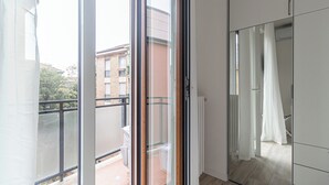 A modern apartment with a sliding glass door leading to a balcony, a view of a building across the street, and a white wardrobe with a mirror. - Italianway Comfort - Serra 16 (Milano)