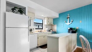 Une cuisine de taille réduite, avec des appareils électroménagers blancs, une fenêtre et un mur d’accent bleu.