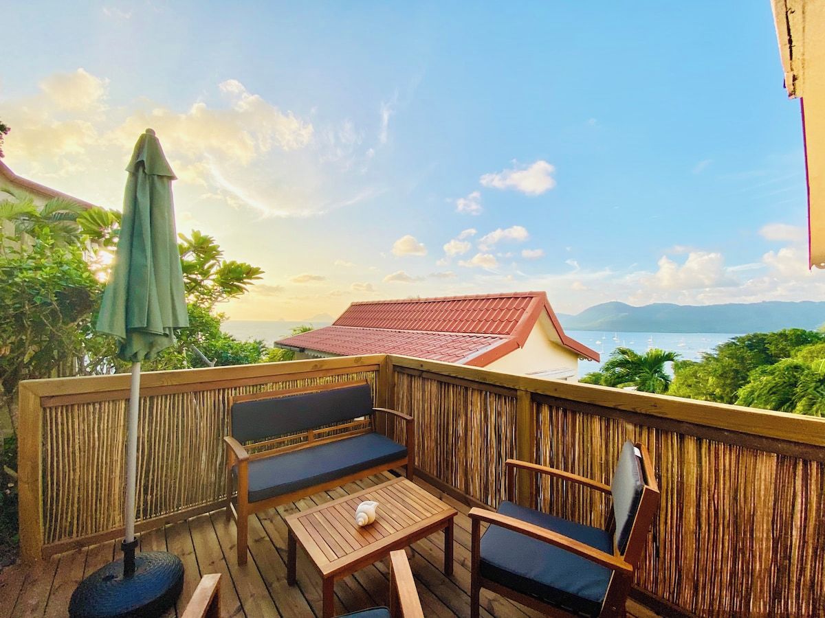 Une terrasse en bois avec un espace salon, une table et un parasol vert.