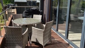 A covered outdoor seating area with wicker furniture and a glass door leading to a deck. - Luxury Lodge Palms 3 with hot tub - Accessible Access (North Connel)