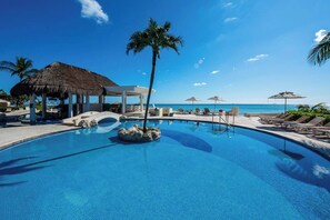 Piscina de resort con sillas de descanso, una palmera y una estructura de techo de paja.