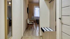 Um corredor com piso de madeira, sala de jantar com mesa e cadeiras, um espelho e um guarda-roupa com cabideiro.