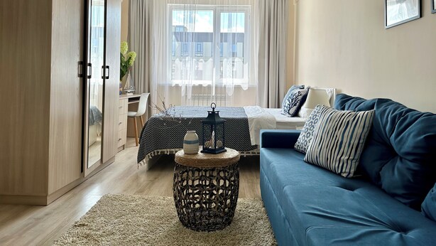 Uma sala de estar moderna com um sofá azul, uma mesa de jantar com toalha de mesa estampada e uma mesinha de vime.