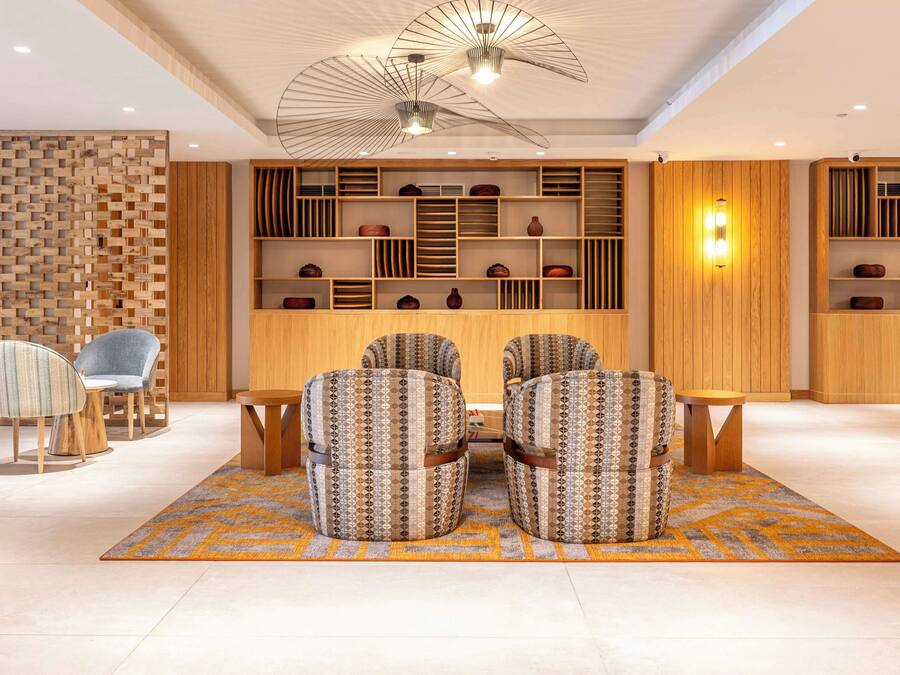 A modern lobby with a seating area, wooden shelving with decorative items, and a patterned rug.