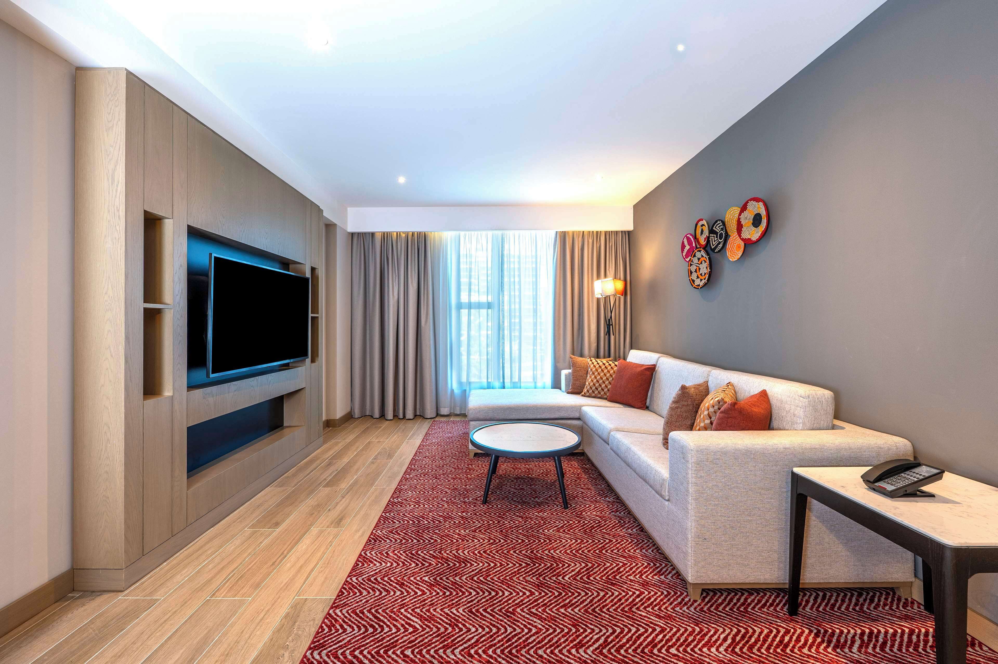 A modern living room with a flat-screen TV, a sofa, a coffee table, and a patterned rug.