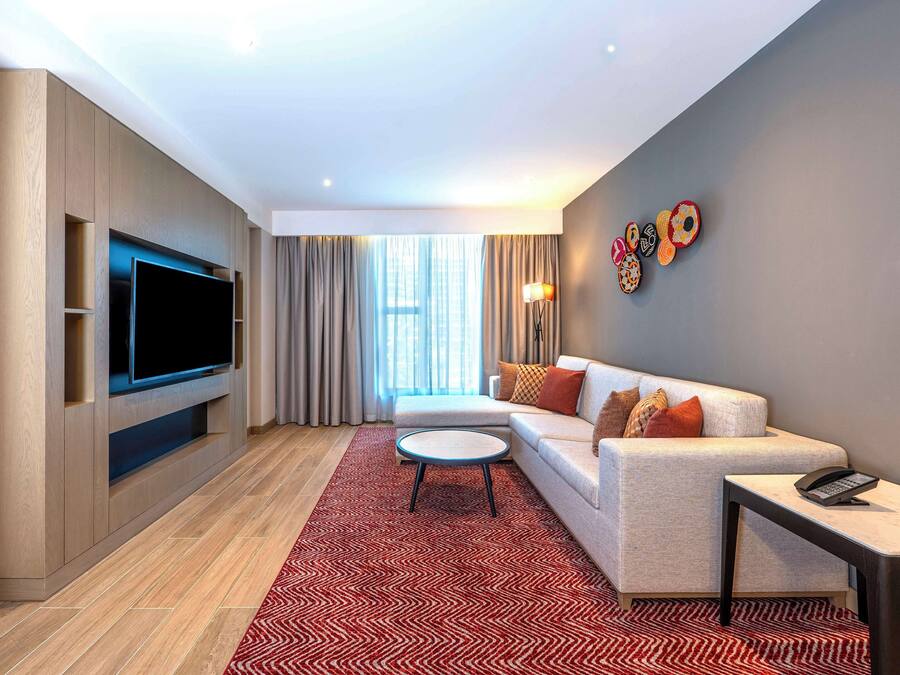 A modern living room with a flat-screen TV, a sofa, a coffee table, and a patterned rug.