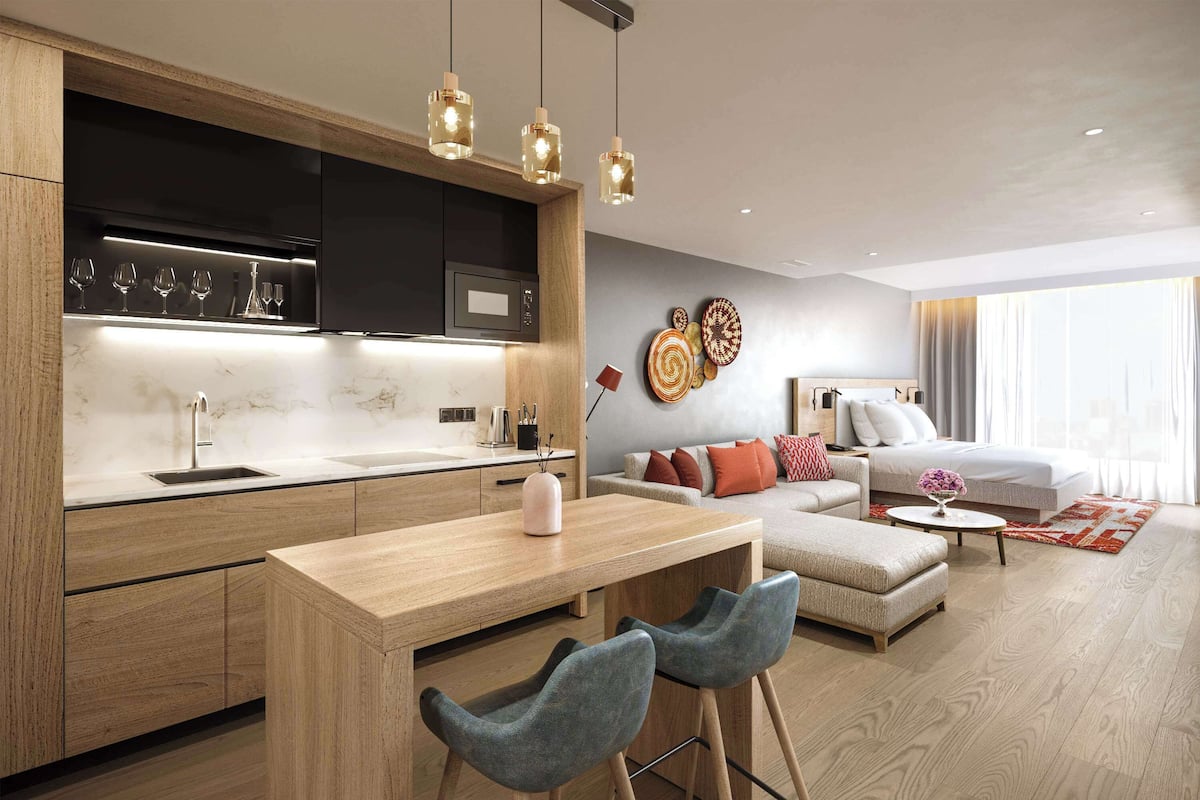 Una cocina moderna con una isla central, taburetes de bar e iluminación colgante. Se ve un área de estar con un sofá y una mesa de centro al fondo.