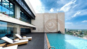 Una piscina infinita en la azotea con sillones de descanso, un muro con diseño y vistas a la ciudad.