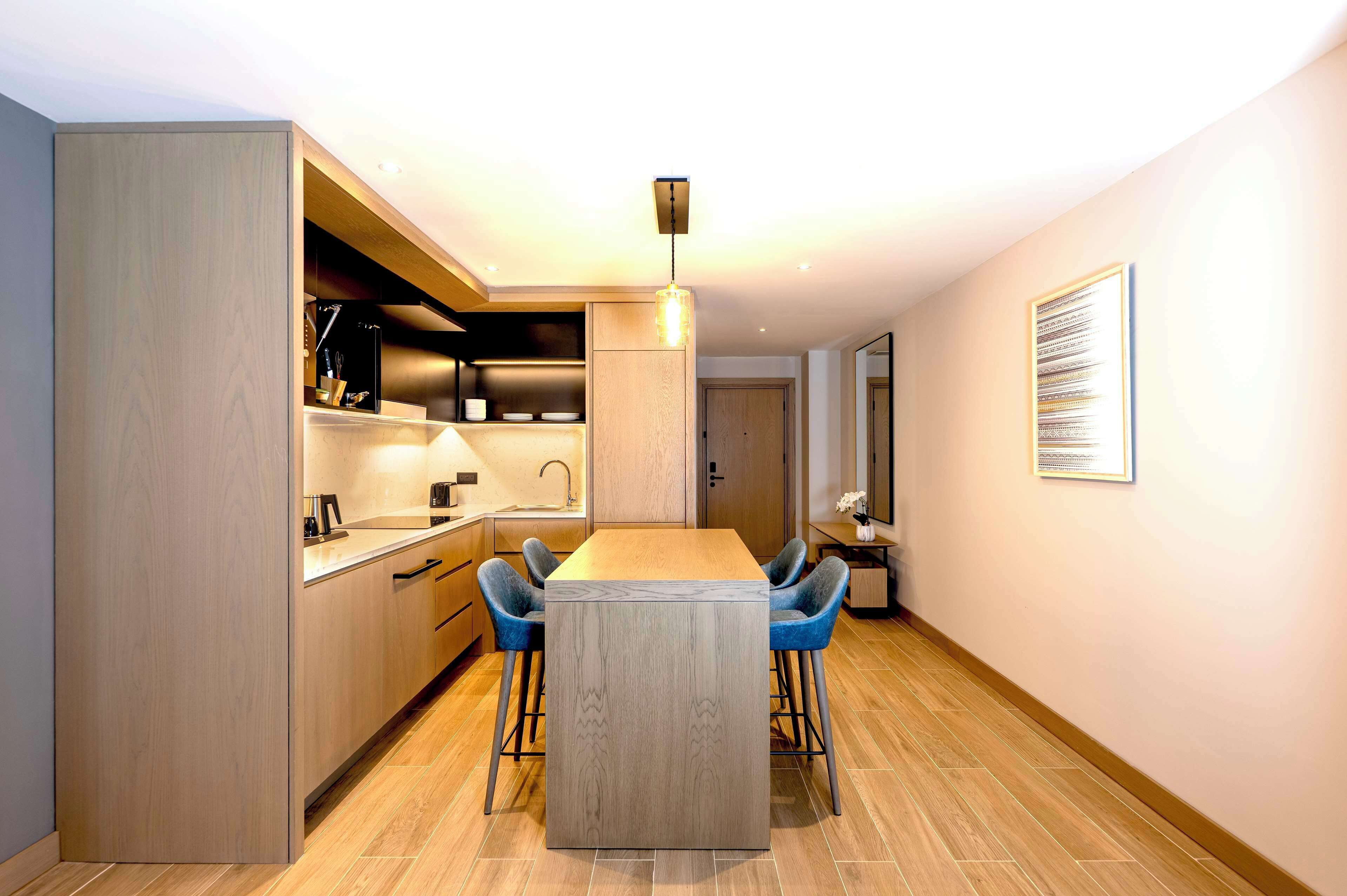 Una cocina moderna con armarios de madera, una isla central, taburetes de bar y una lámpara colgante.
