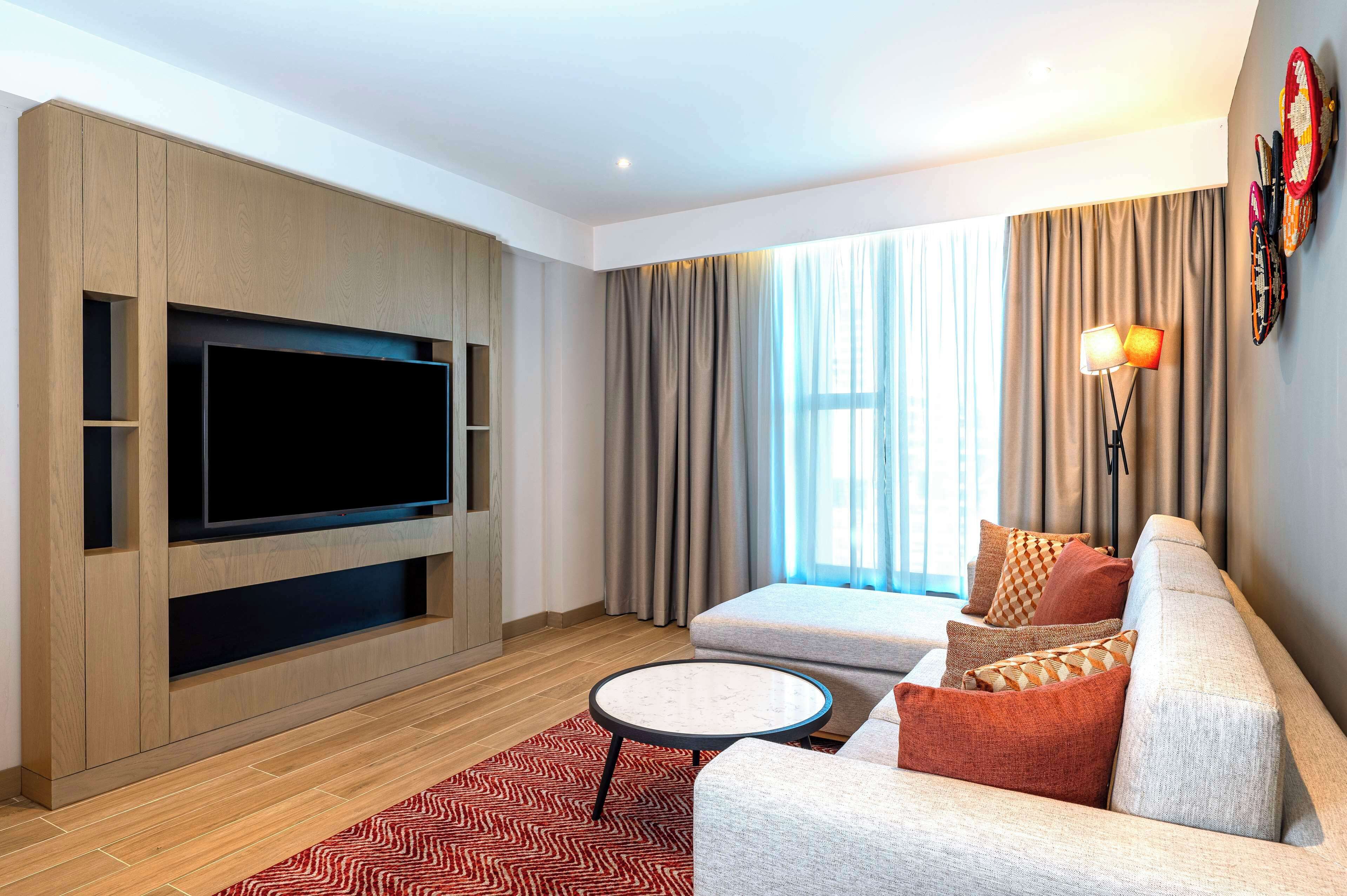 A modern living room with a flat-screen TV, a sofa, a coffee table, and a patterned rug.