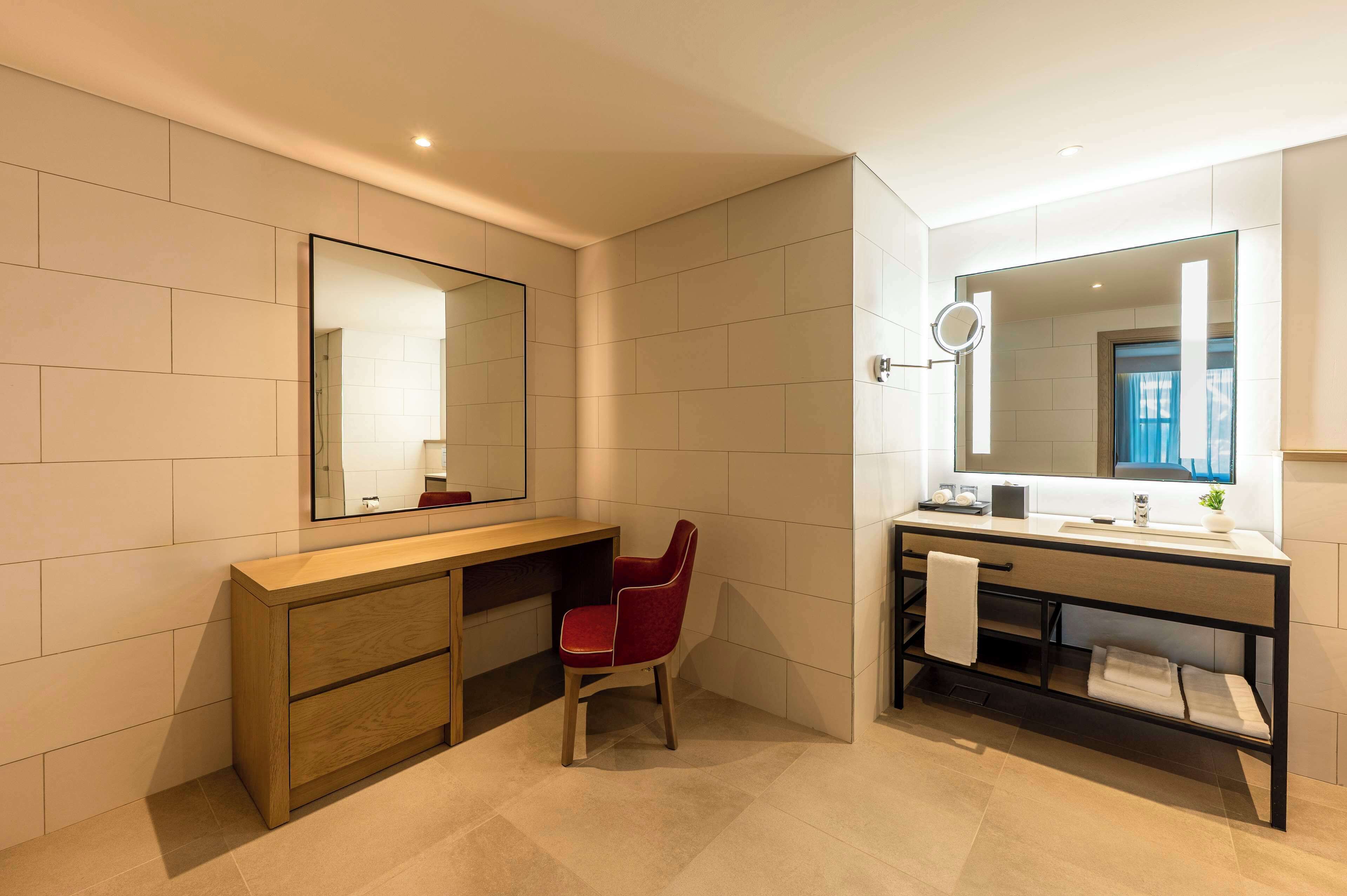 A modern bathroom with a wooden vanity, a red chair, a large mirror, and a built-in sink.