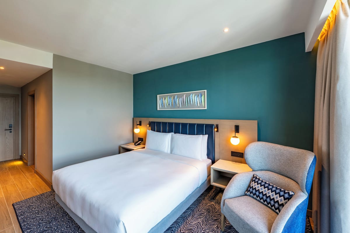Habitación de hotel con una cama grande, una silla, una mesita de noche y un aplique de pared.