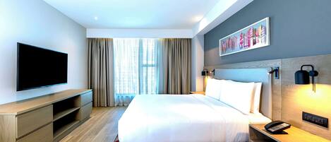 Habitación de hotel moderna con una cama grande, un televisor de pantalla plana, una mesita de noche de madera y una lámpara fijada a la pared.
