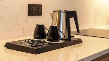 A coffee station with a kettle, two coffee cups, and a tray with various coffee pods and utensils.