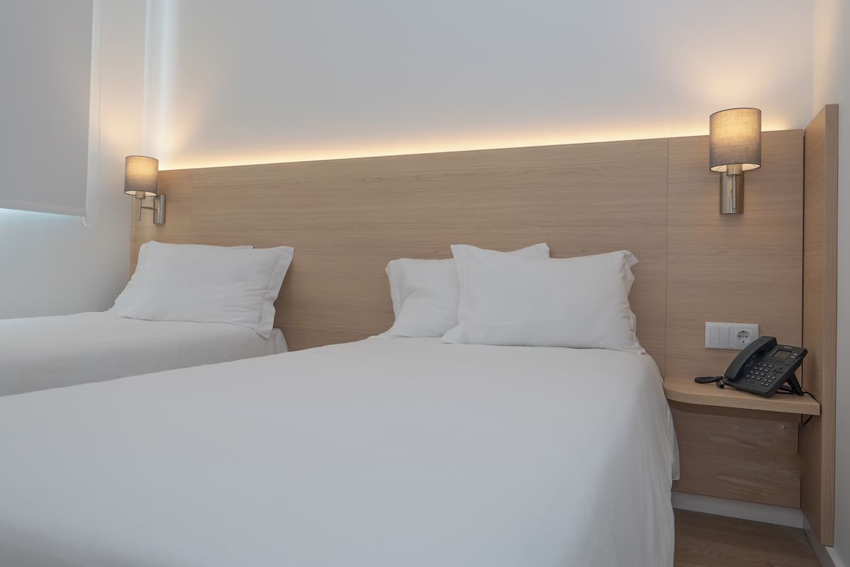 Hotellihuoneessa on kaksi erillistä sänkyä, joissa on valkoiset lakanat ja tyynyt. Sänkyjen molemmilla puolilla on seinään kiinnitetyt lamput. Puinen yöpöytä on sijoitettu sänkyjen viereen, ja sen päälle on asetettu puhelin.