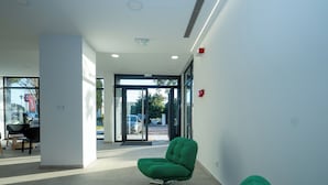 Un intérieur moderne avec un fauteuil recouvert d’un tissu vert, un fauteuil noir et une porte en verre donnant sur l’extérieur.