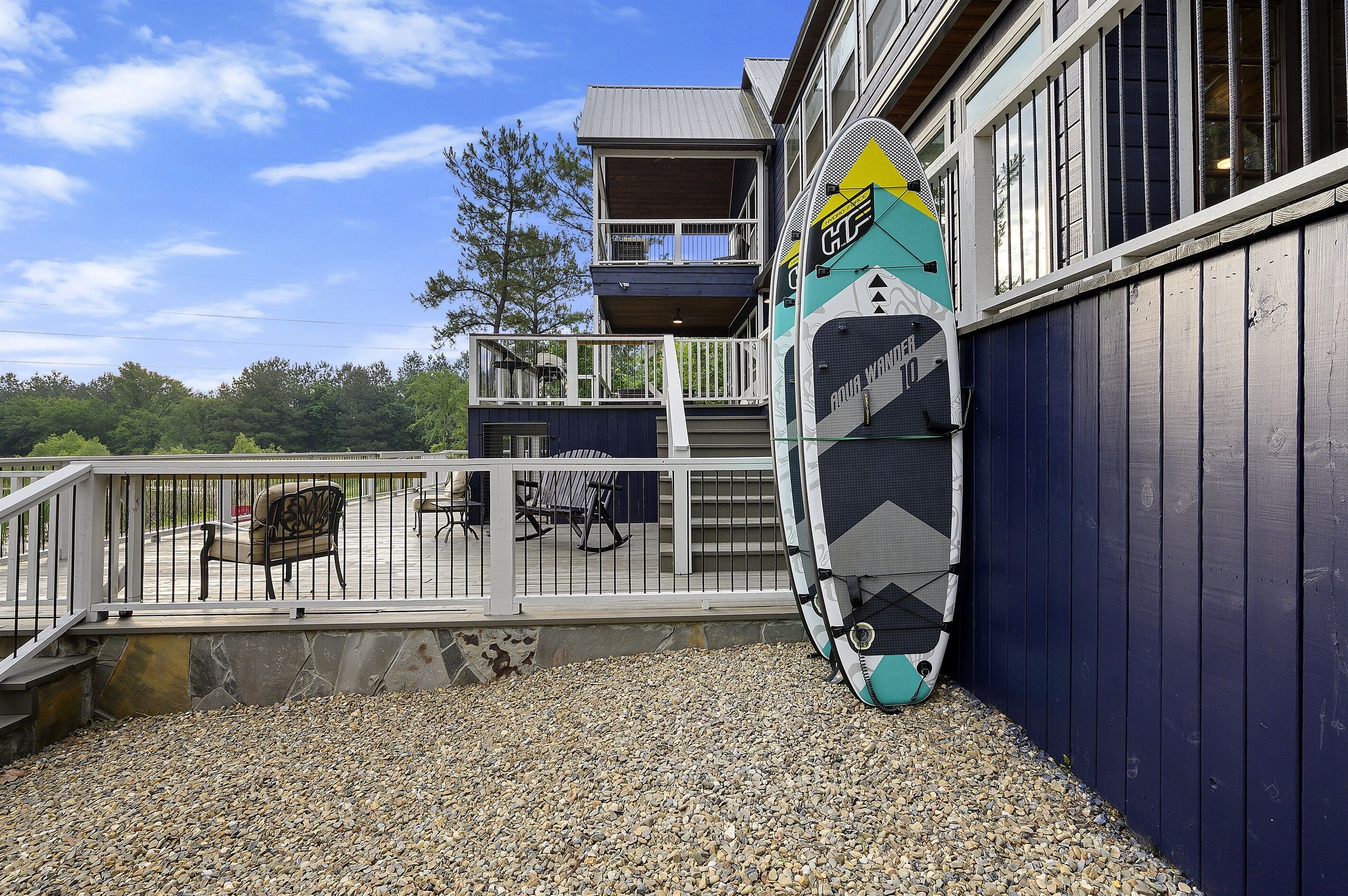 Een gebouw met een balkon, een surfboard tegen de muur en een grindpad.