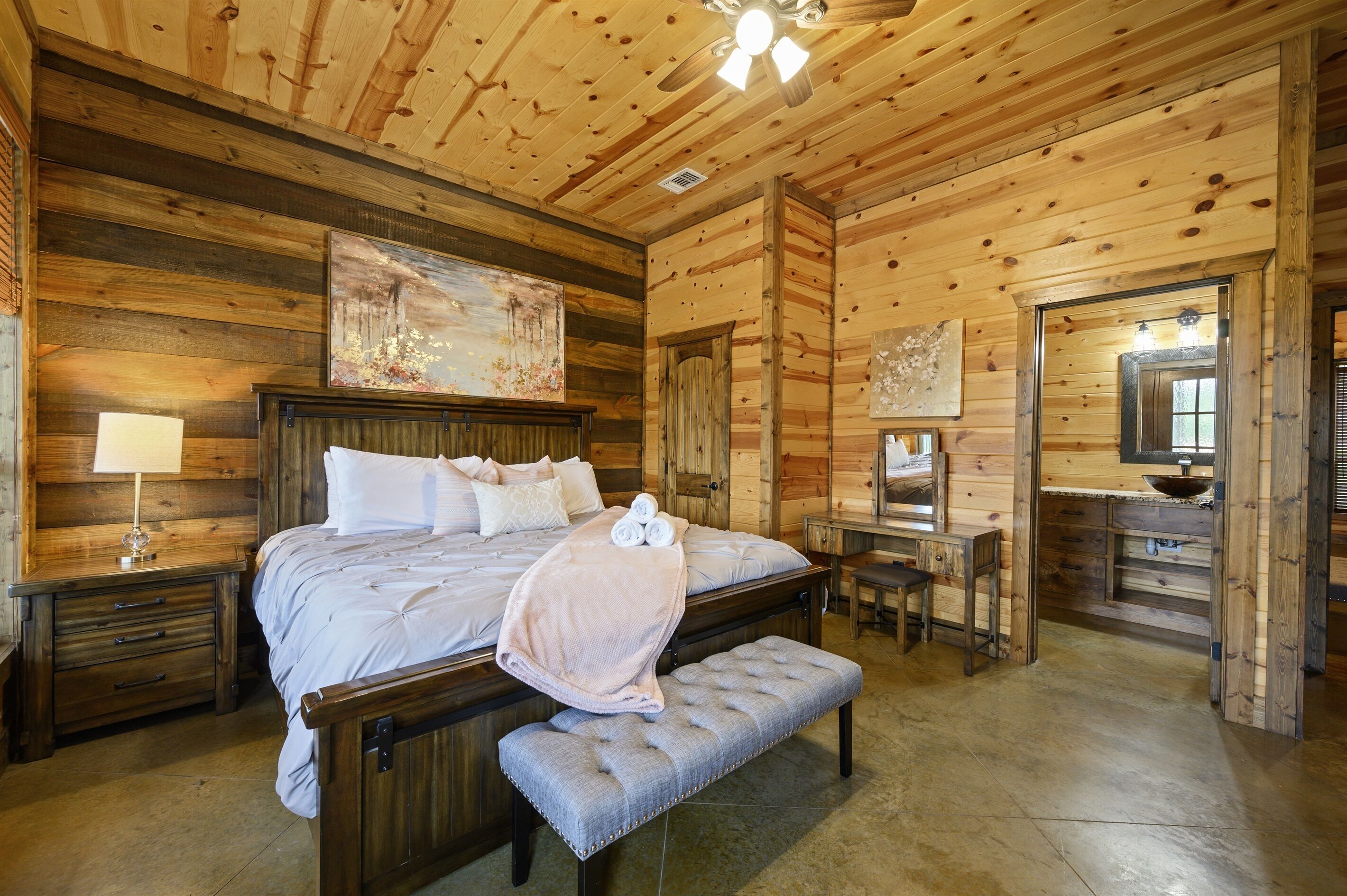 A wooden cabin-style bedroom with a large bed, a bench, a desk, and a mirror.