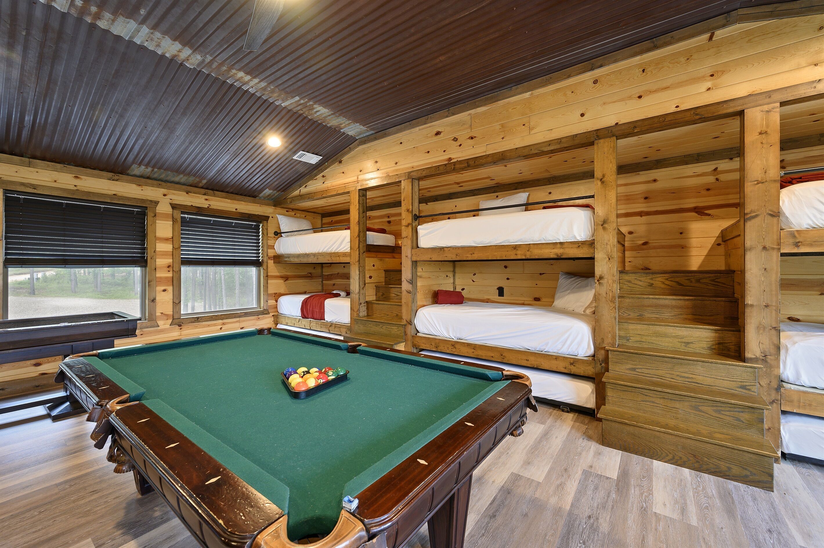 A pool table with a ball rack in a wooden room with bunk beds and a window.