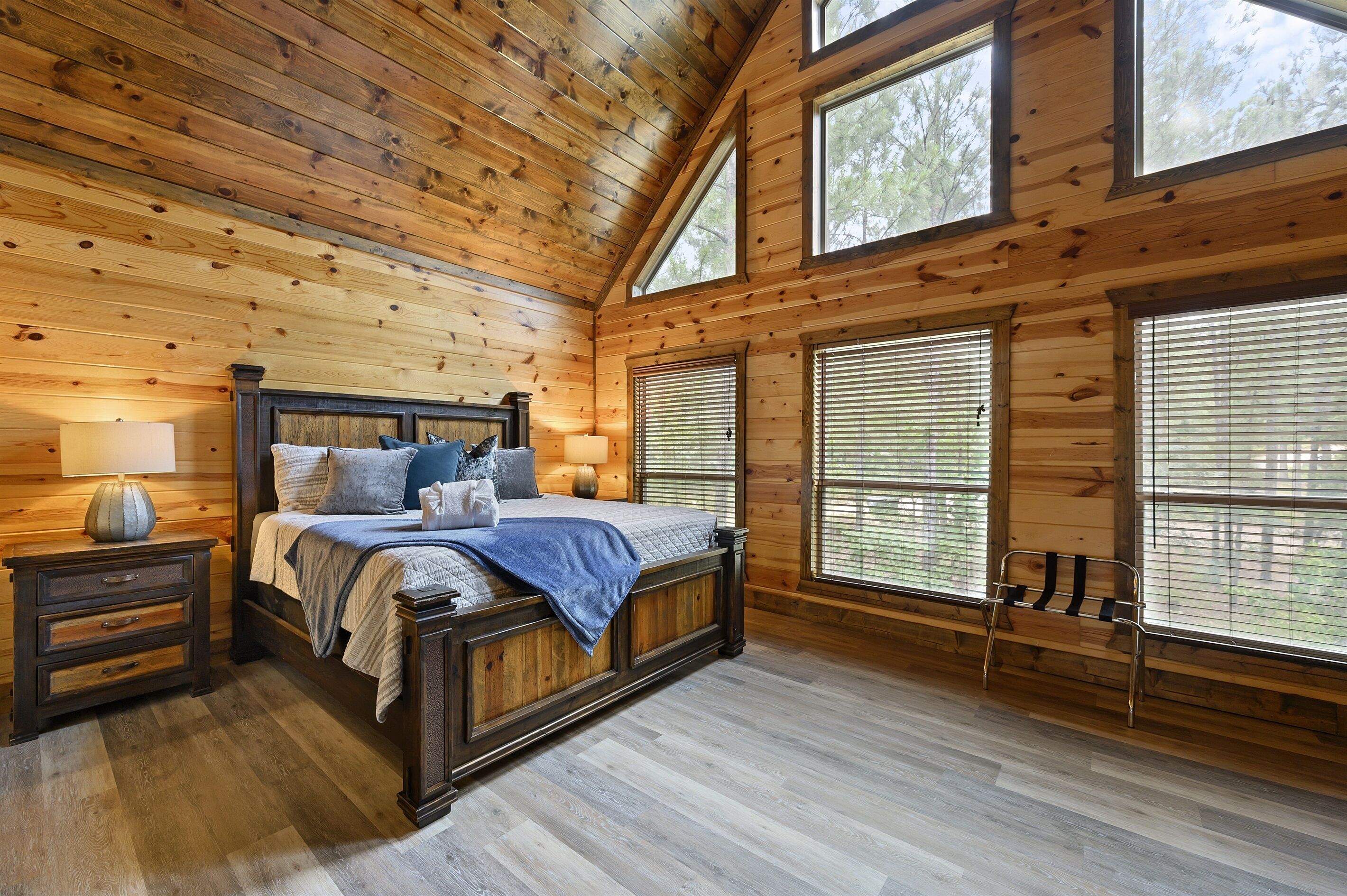 A wooden-paneled bedroom with a bed, nightstands, and large windows.