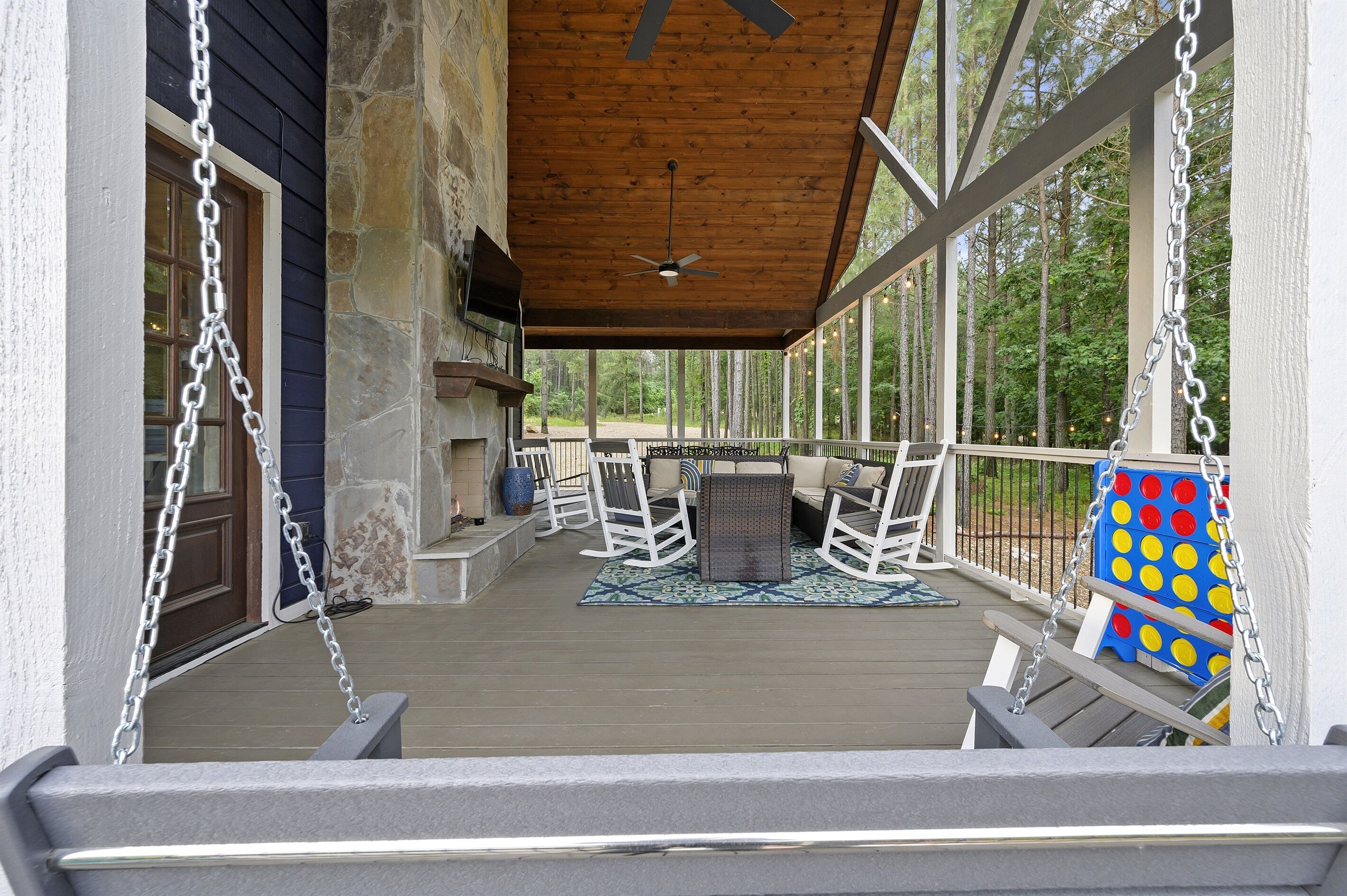 A covered porch with a ceiling fan, a stone wall, and a view of the forest.