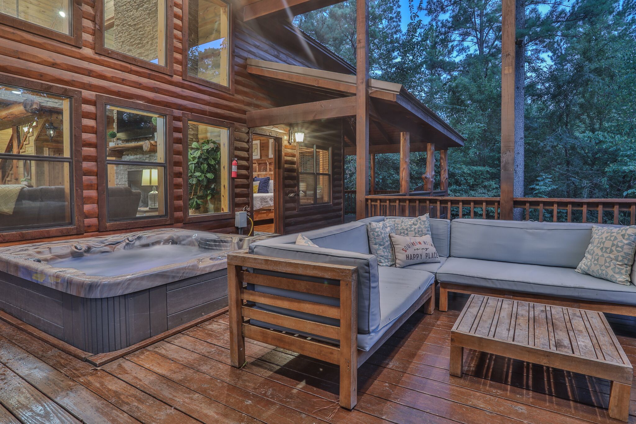 A wooden cabin with a hot tub, a sofa, and a wooden table on a deck.