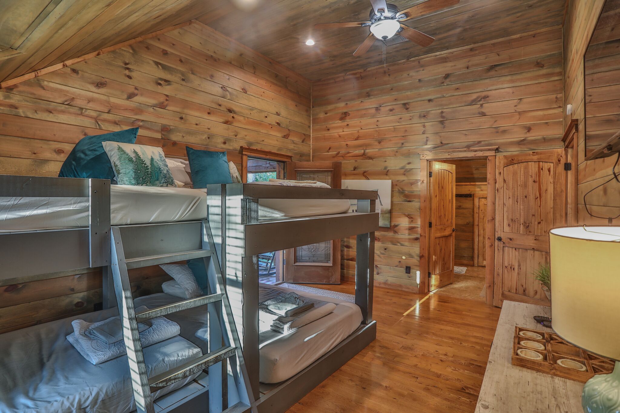 A wooden cabin with bunk beds, a ceiling fan, and a wooden door.