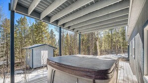 A hot tub on a wooden deck with a view of a forest and a small shed in the background.
