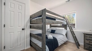 A bunk bed with a wooden frame, white bedding, and a ladder.