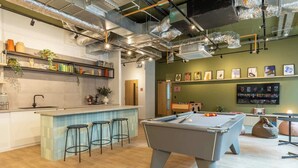 A modern bar area with a pool table, bar stools, and a counter with shelves of books and decorative items. - Student Only The Waterways (Nottingham)