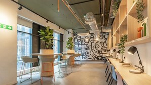 A modern office space with round tables and chairs, a patterned wall, and shelves with plants and books. - Student Only The Waterways (Nottingham)