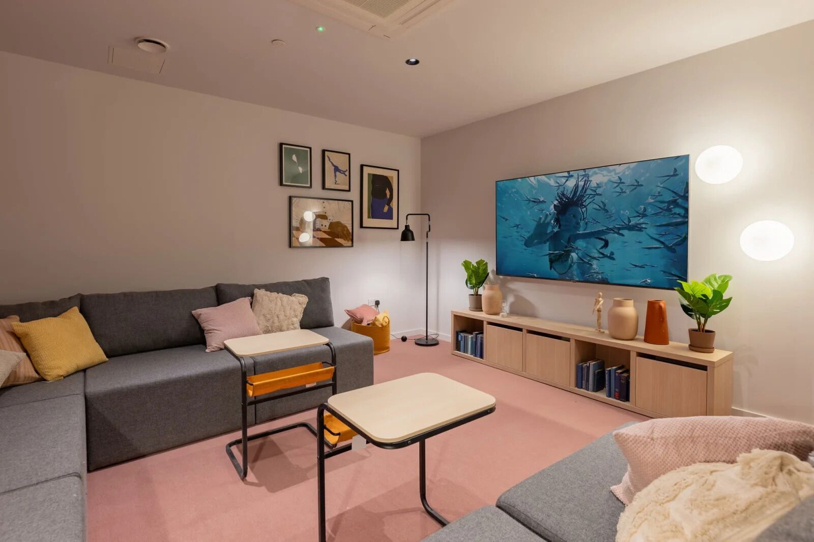 A modern living room with a grey sofa, a small table, a bookshelf, and a large painting on the wall.