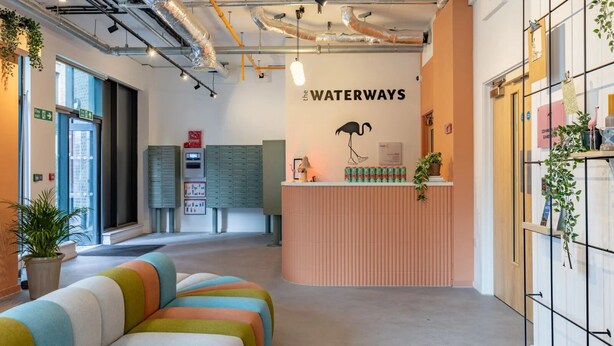A modern reception area with a colorful sofa, a reception desk, and a wall-mounted sign reading "the WATERWAYS". - Student Only The Waterways (Nottingham)