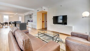 Un salon moderne comprenant un ensemble de canapés, une table basse en verre et un téléviseur à écran plat fixé sur un meuble blanc.