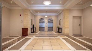 Un hall d’entrée spacieux avec un sol à motifs en damier, deux ascenseurs et une porte sur le côté droit.