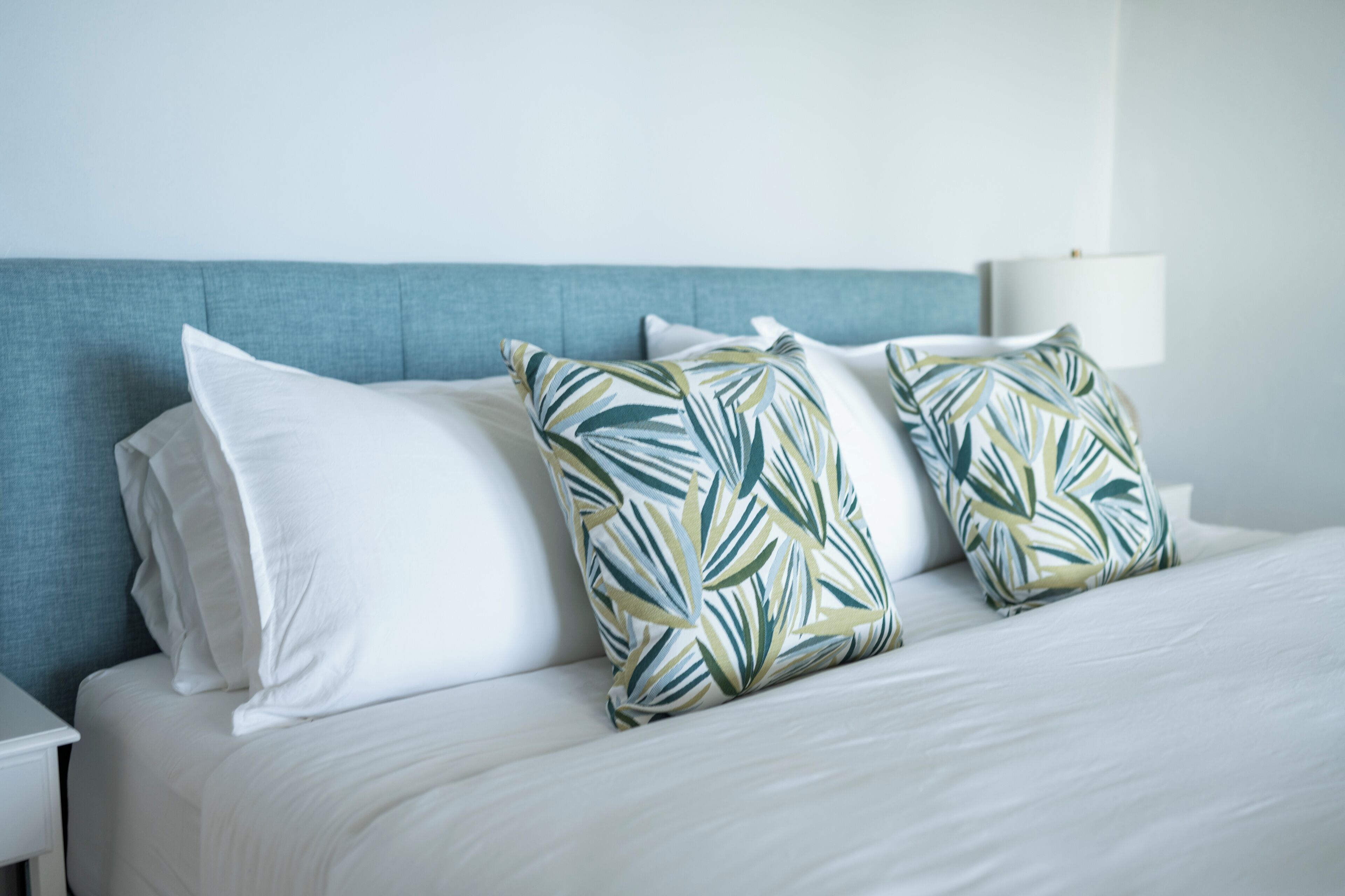 A neatly made bed with white linens and two decorative pillows with a leaf pattern.