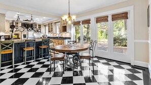 A kitchen with a checkered floor, a central island with stools, and a dining table with chairs. - Spacious Historic Manor with Chef's Kitchen • Horse-Friendly (Southern Pines)