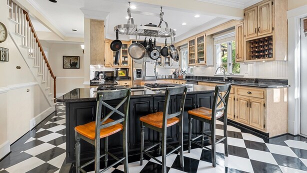 A kitchen with a central island, bar stools, hanging pots, and a checkered floor. - Spacious Historic Manor with Chef's Kitchen • Horse-Friendly (Southern Pines)