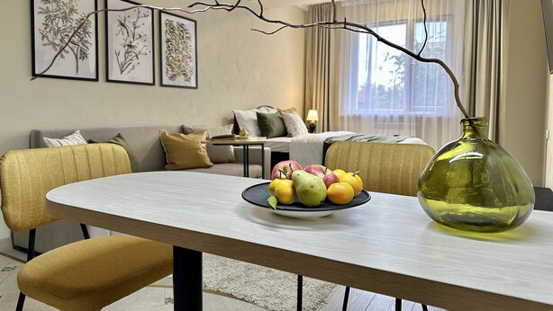 Un coin repas comprenant une table, des chaises, un vase et un panier de fruits.