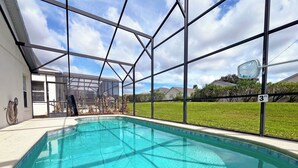 A swimming pool with a clear blue water, surrounded by a glass enclosure with a metal frame, and a view of a grassy yard and houses in the background. - Highgate Haven - Bright pool home with games room in gated community (Davenport)