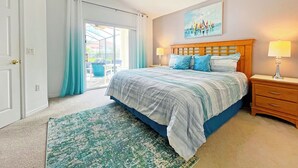 A bedroom with a bed, two bedside tables, a ceiling fan, a painting, and a view through a sliding door to an outdoor area. - Highgate Haven - Bright pool home with games room in gated community (Davenport)
