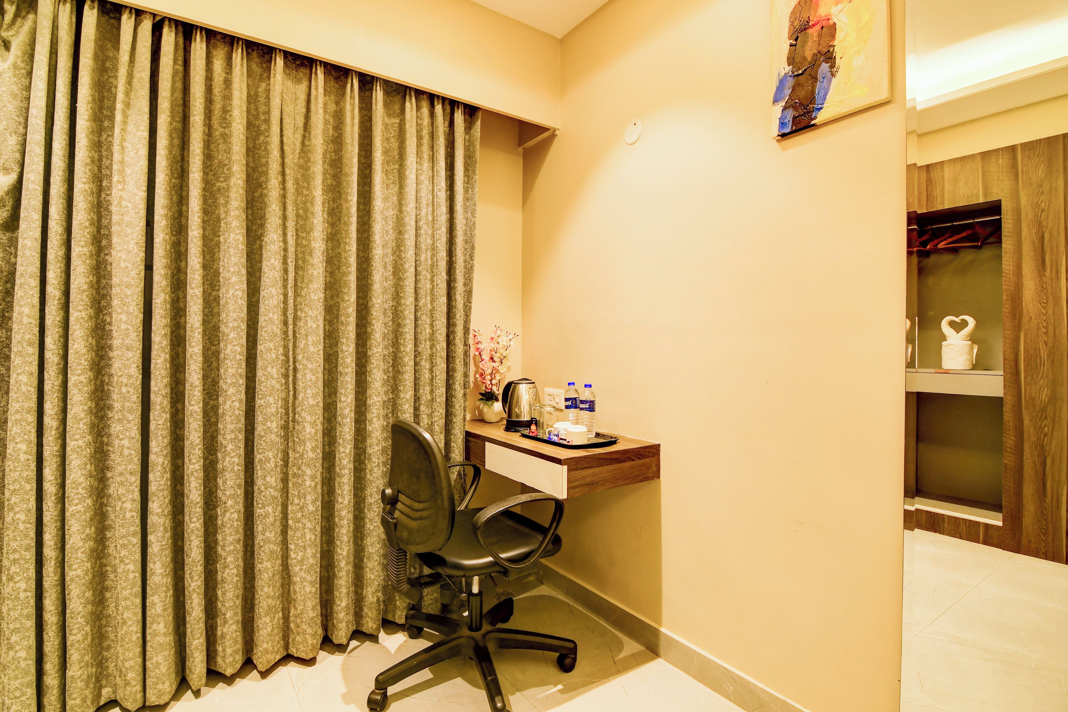 A hotel room with a desk, chair, and a small shelf with toiletries.