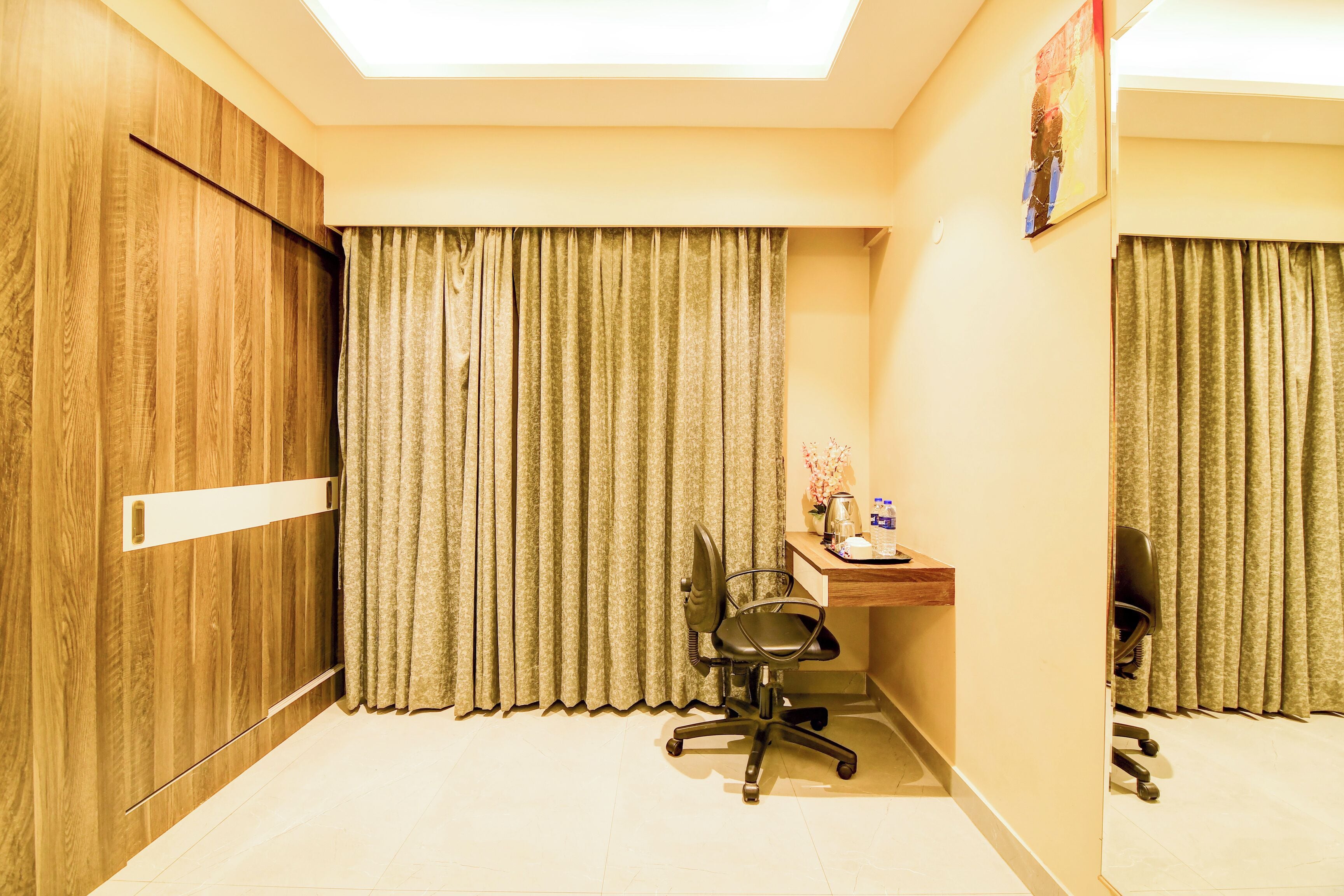 A room with a wooden wardrobe, a desk with a chair, and a large window with curtains.