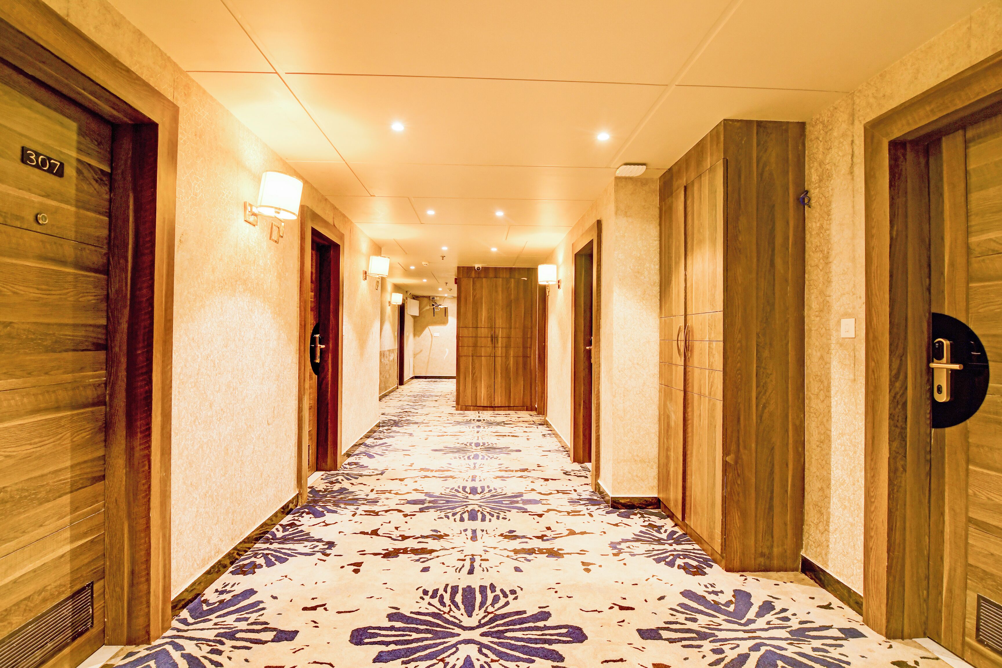 A hotel hallway with wooden doors, numbered 307, and a patterned carpet.
