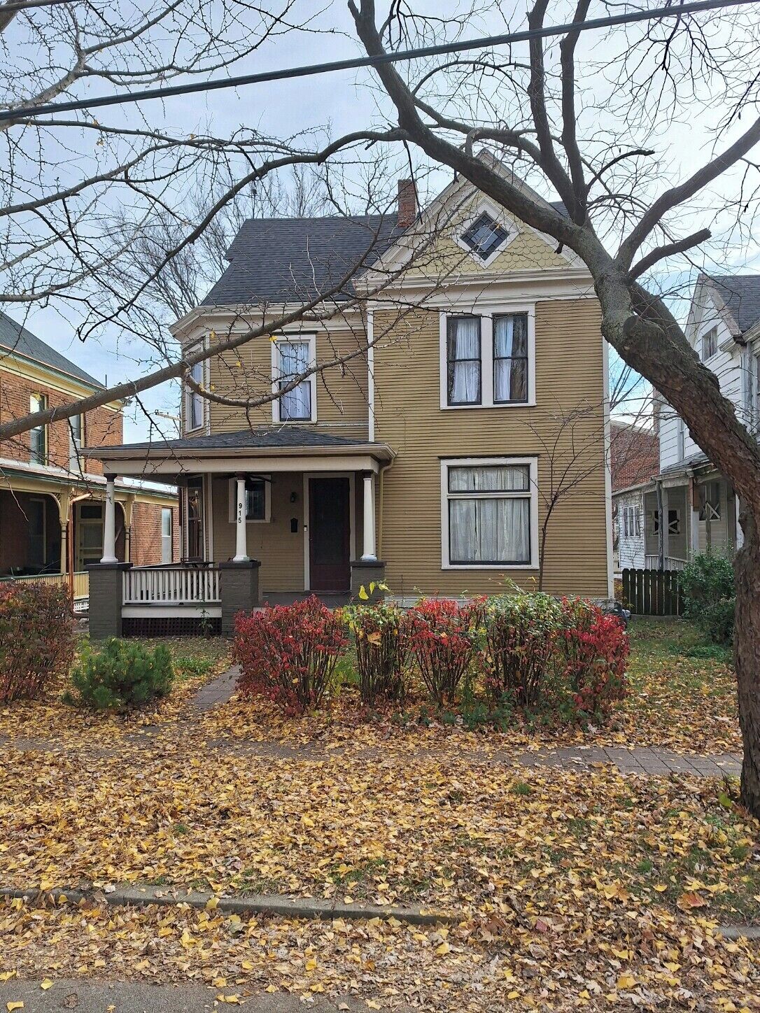 A two-story house with a front porch, a chimney, and a small garden with shrubs.